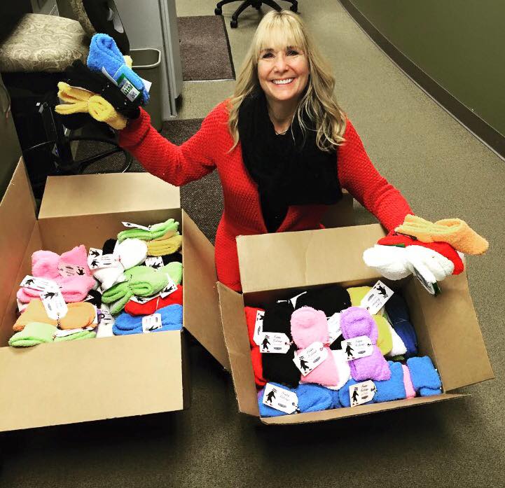 woman kneeled down in front of boxes of fuzzy socks holding some up